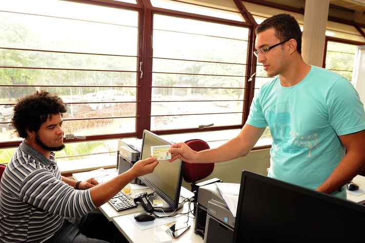 Estudante Rafael Martins Ribeiro (à direita) recebe a carteira, que lhe dará acesso às unidades acadêmicas da UFMG