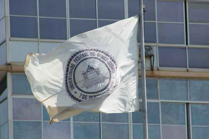 Bandeira da UFMG em primeiro plano com prédio da Reitoria ao fundo