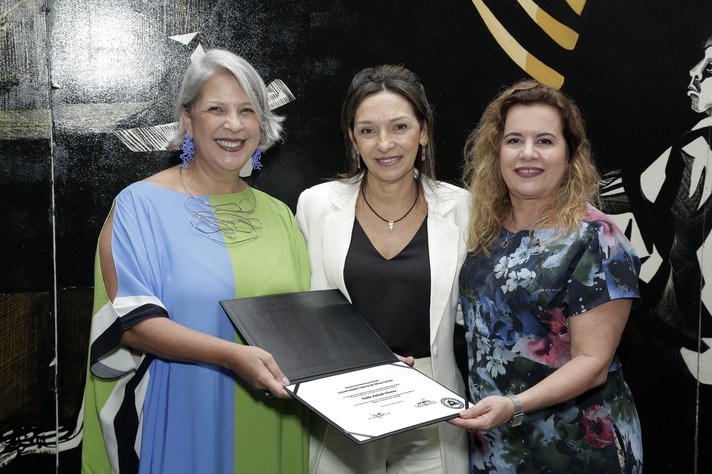 Dalila Oliveira, ao centro, recebe diploma de professora emérita das mãos da diretora da FAE, Andrea Moreno e da reitora, Sandra Goulart Almeida