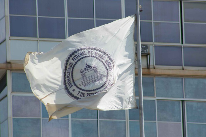 Bandeira da UFMG em primeiro plano com prédio da Reitoria ao fundo