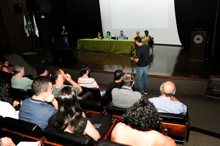 Mesa para a interlocução com os participantes foi composta por Bruno (de azul), Maria José Flores, pró-reitora adjunta (verde), e por membros do Grupo de Trabalho (GT) responsável pela pesquisa que embasa a concepção da proposta