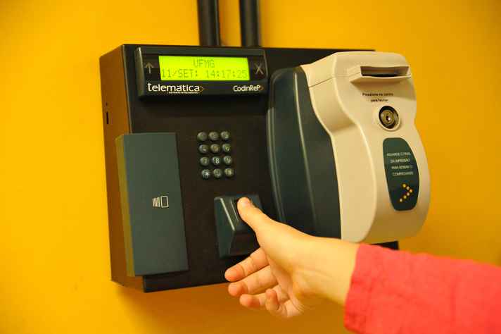 Foto de uma pessoa colocando o dedo polegar no dispositivo de registro do ponto eletrônico da UFMG 