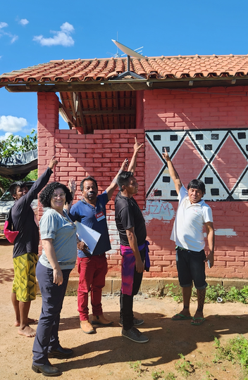 A professora Vanessa Tomaz e indígenas Maxakali mostram o Starlink instalado no alto do centro comunitário da aldeia